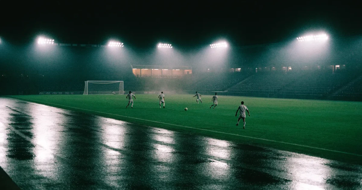 Ein großes Fußballstadion bei Flutlicht von außen, davor ein leerer Vorplatz mit nassem Pflaster und Dunst.