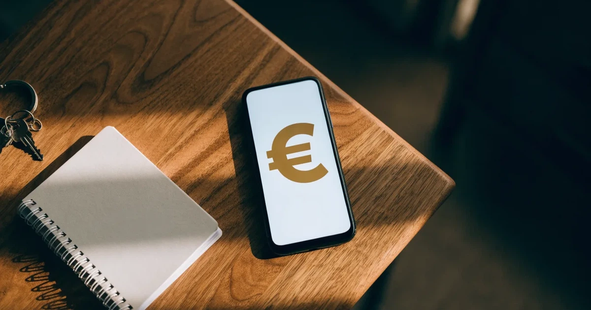 Ein Handy mit abgedunkeltem Display, ein Schlüsselbund und ein Notizblock liegen auf einem Holztisch.