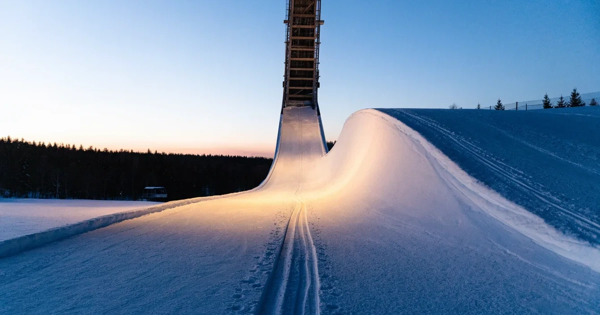 Eine Skisprungschanze im Schnee, von unten gesehen, vor einem klaren Winterhimmel in der Dämmerung, ohne Menschen.