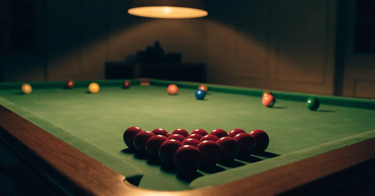 Ein Snookertisch mit grünem Tuch und aufgebauten roten Kugeln in einem abgedunkelten Raum unter einer hängenden Lampe.