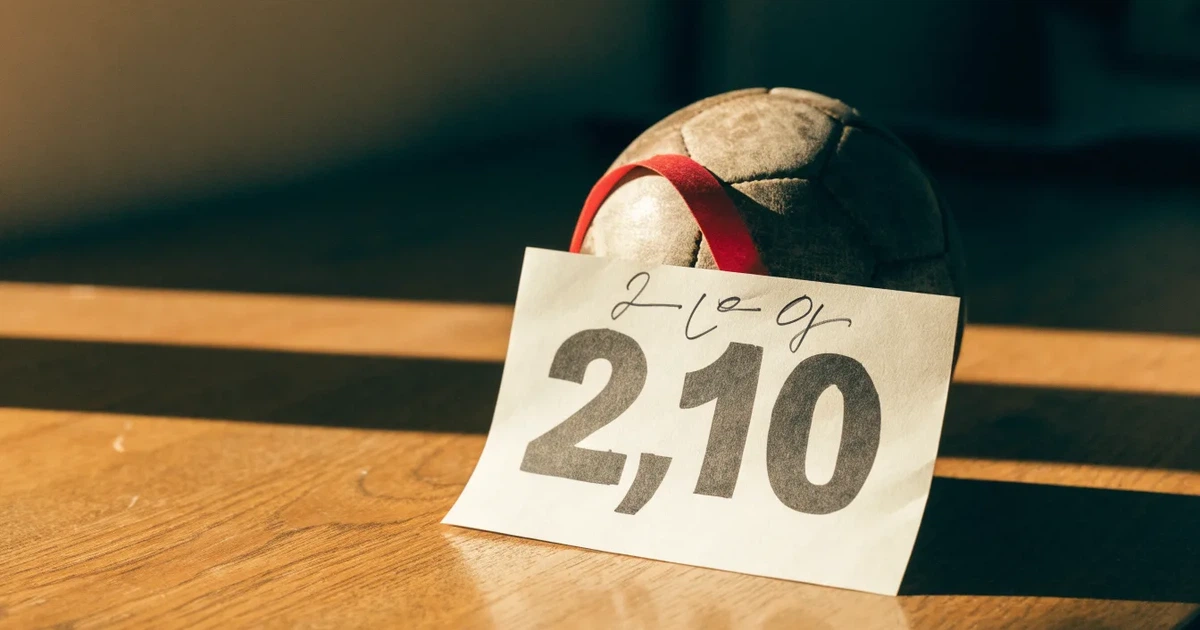 Ein kleines Geschenkband liegt neben einem Fußball und einem leeren Papier-Wettschein auf einem Holztisch im Tageslicht.
